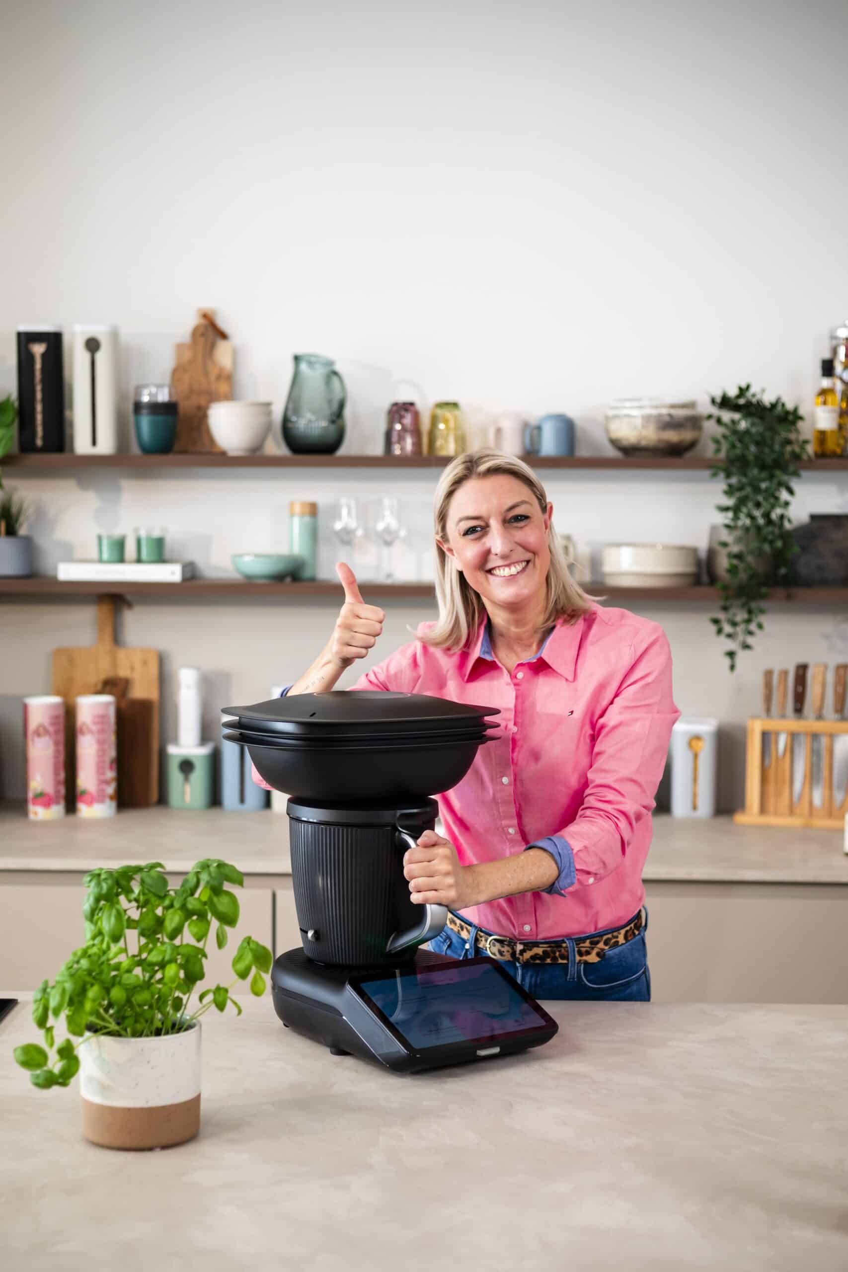 D&eacute;si aus dem Zaubertopf Team zeigt den Daumen nach oben w&auml;hrend sie neben einem Thermomix 7 in schwarz steht